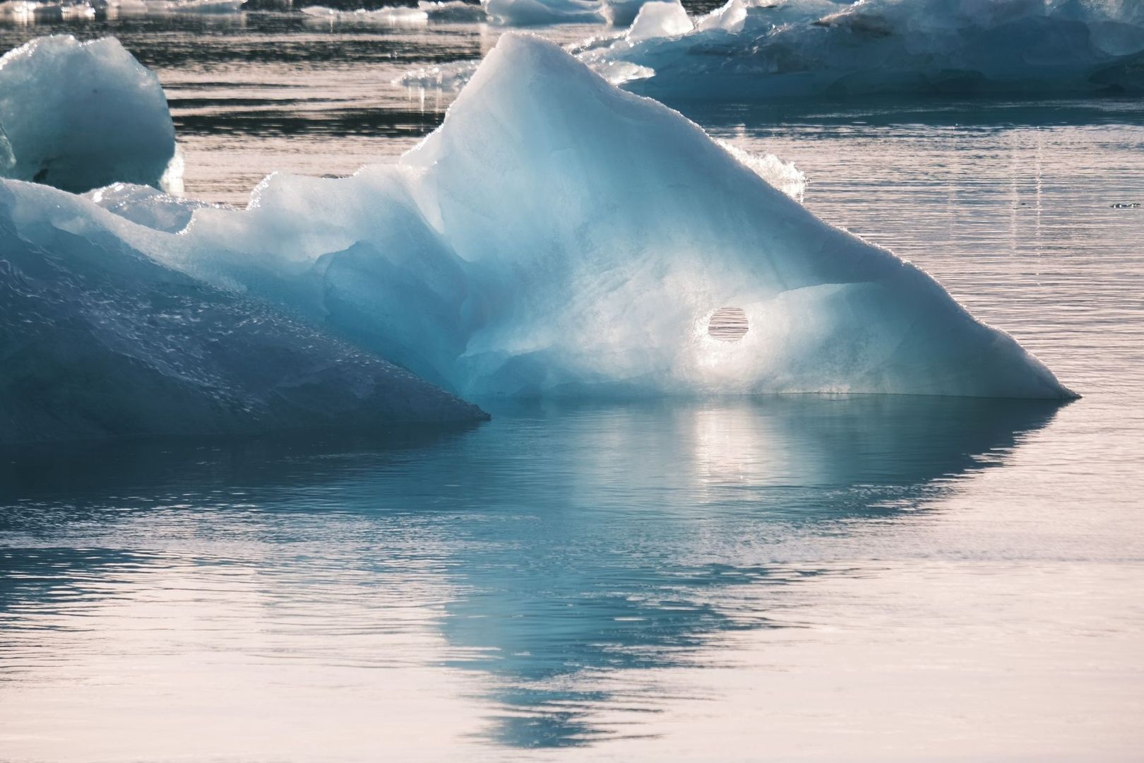 Blau schimmernder Eisberg treibt in ruhigem Wasser